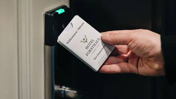 A hand holding a hotel key card with the name "HOTEL FORSTHAUS" visible.