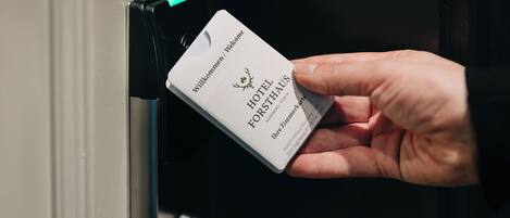 Une main tenant une carte-clé d’hôtel sur laquelle on peut lire le nom « HOTEL FORSTHAUS ».