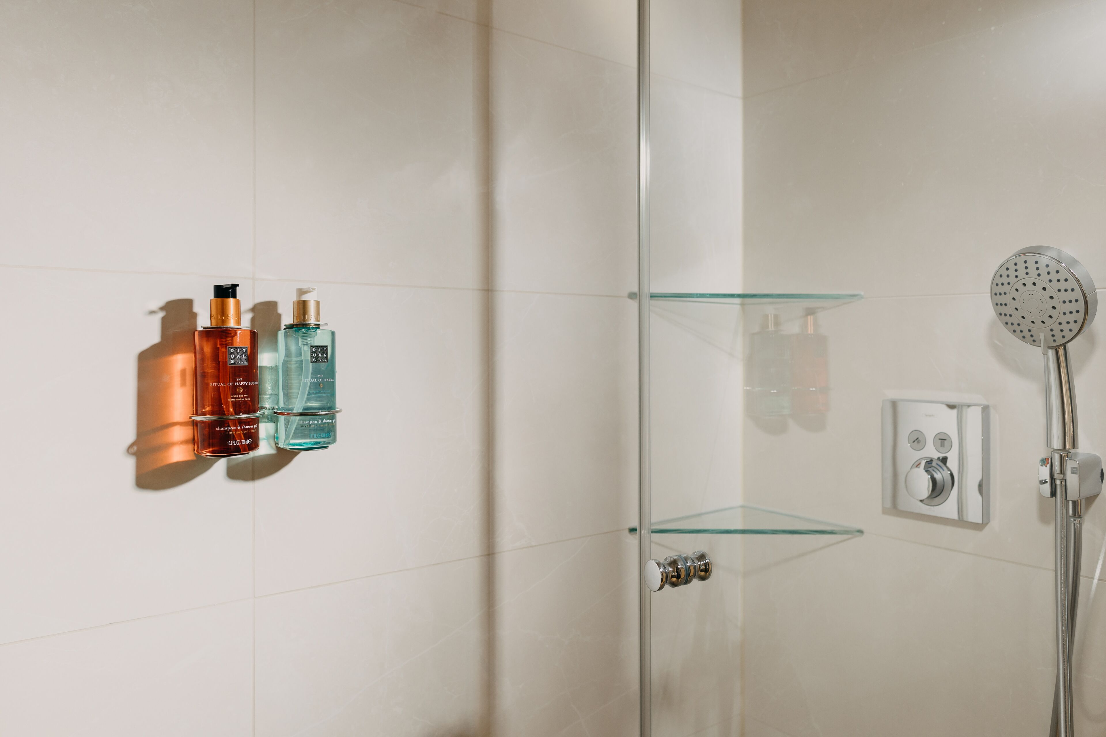 A modern bathroom with a glass shower enclosure, a handheld showerhead, and a wall-mounted control panel.