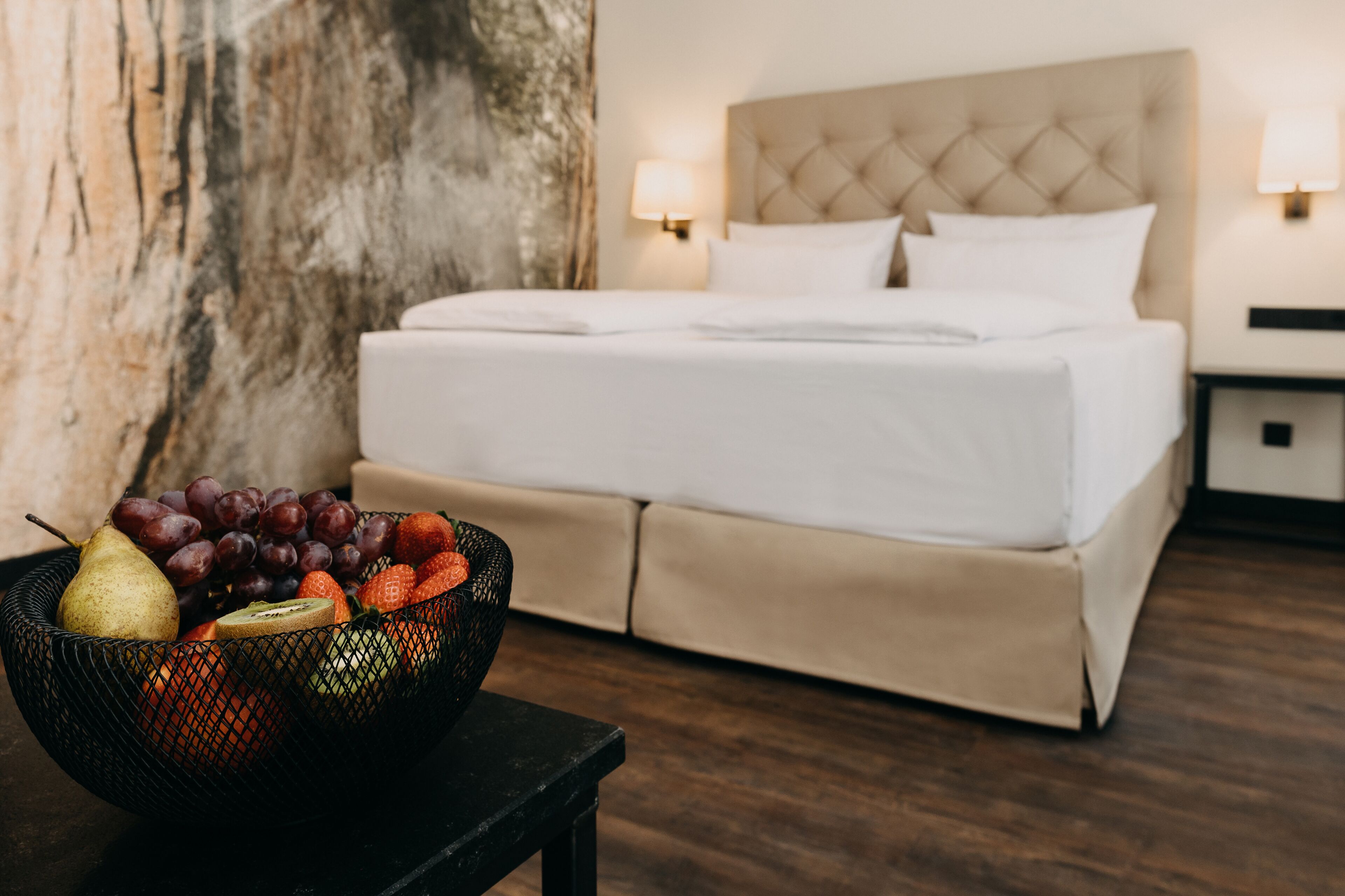 A hotel room with a bed, a fruit bowl on a table, and a wooden wall.