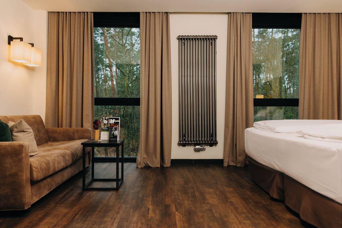 Una camera d'albergo con pavimento in legno, un divano, un letto, un comodino e una finestra con tende.