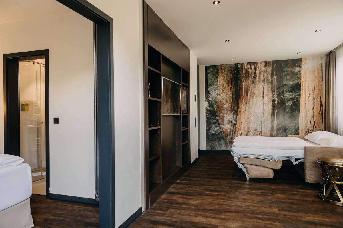 Una moderna camera d'albergo con un ampio armadio, un letto, un'area salotto e una parete con effetto legno.