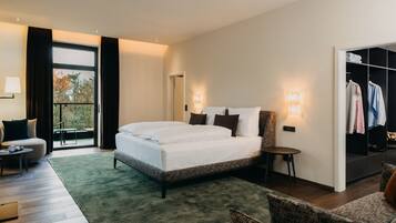 Habitación de hotel moderna con una cama grande, zona de estar con una mesa, armario y vistas al exterior.