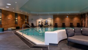 Una piscina interior con barandilla de vidrio, sillas de descanso y un diseño moderno con detalles de madera.