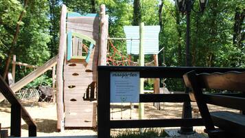 Ein Spielplatz mit einer hölzernen Kletterkonstruktion, einer Rutsche und einer Bank.