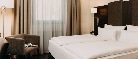 Een hotelkamer met een bed, een stoel, een lamp en een raam met gordijnen.