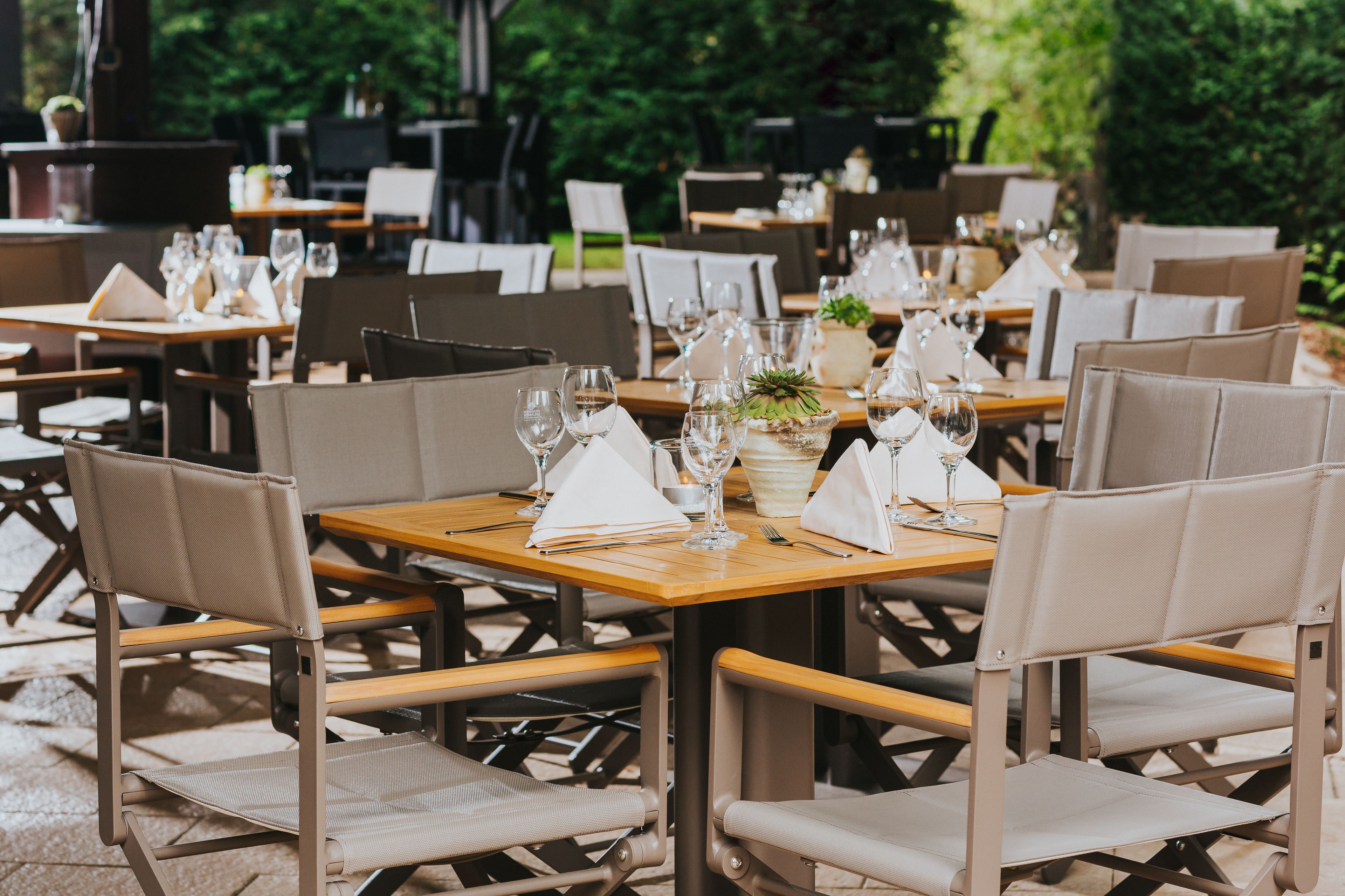 An outdoor dining area with tables set for two, each with a chair, a vase, and a bottle of water.