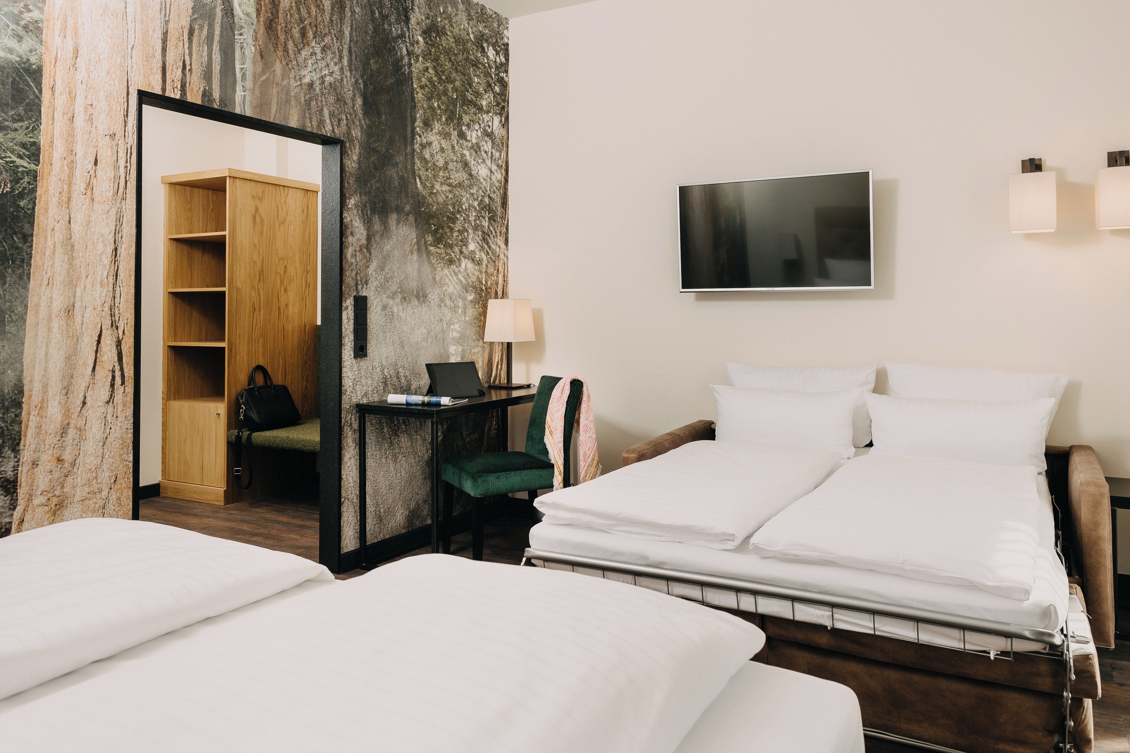 Ein Hotelzimmer mit einem Bett, einem Schreibtisch mit Stuhl, einem Fernseher und einem Kleiderschrank.