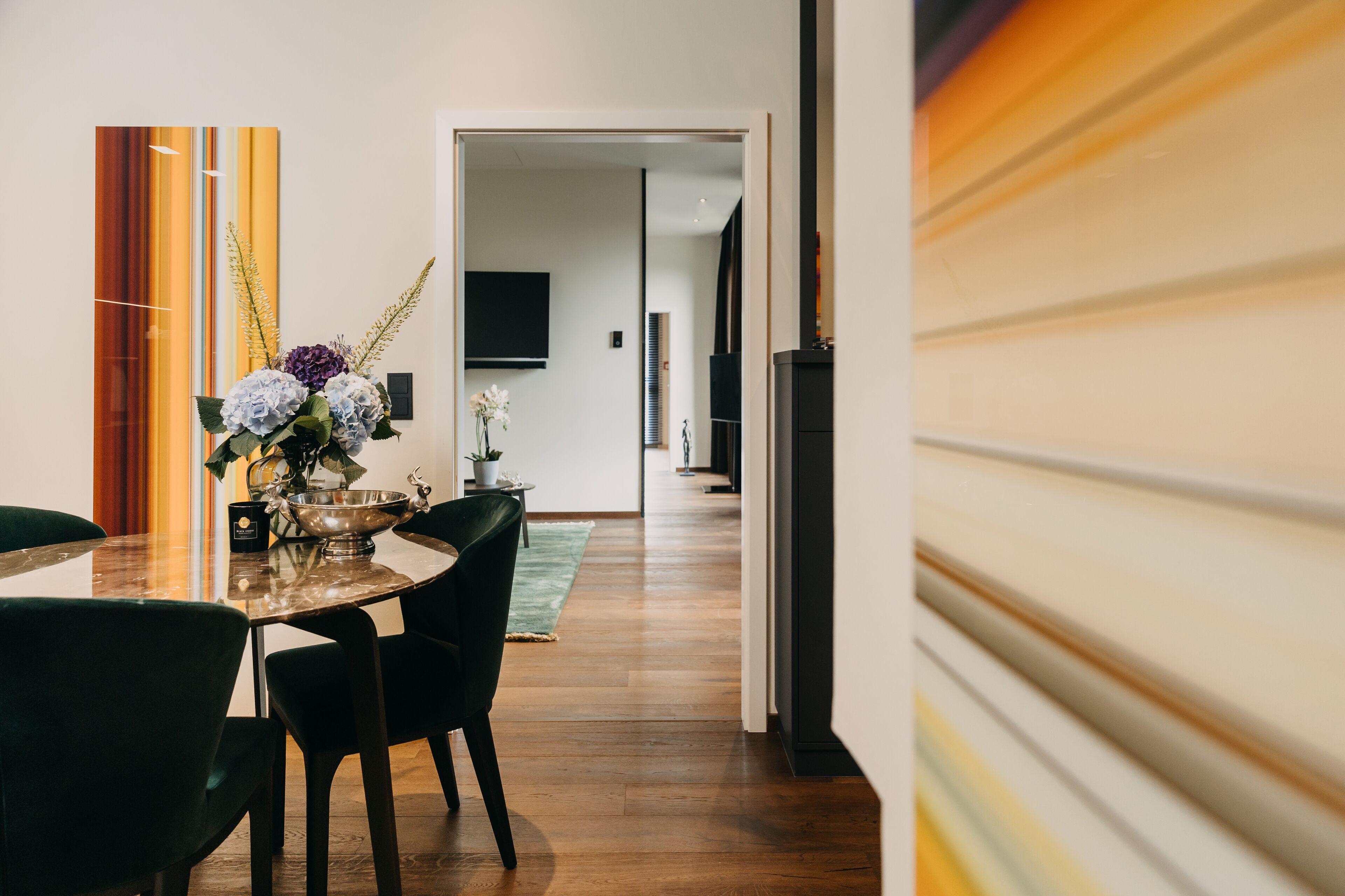 Un comedor moderno con una mesa de madera, sillas verde oscuro y un florero con flores.