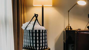 Un sac à carreaux posé sur un petit tabouret, près d’une lampe et d’un mur sur lequel est accroché un rideau.