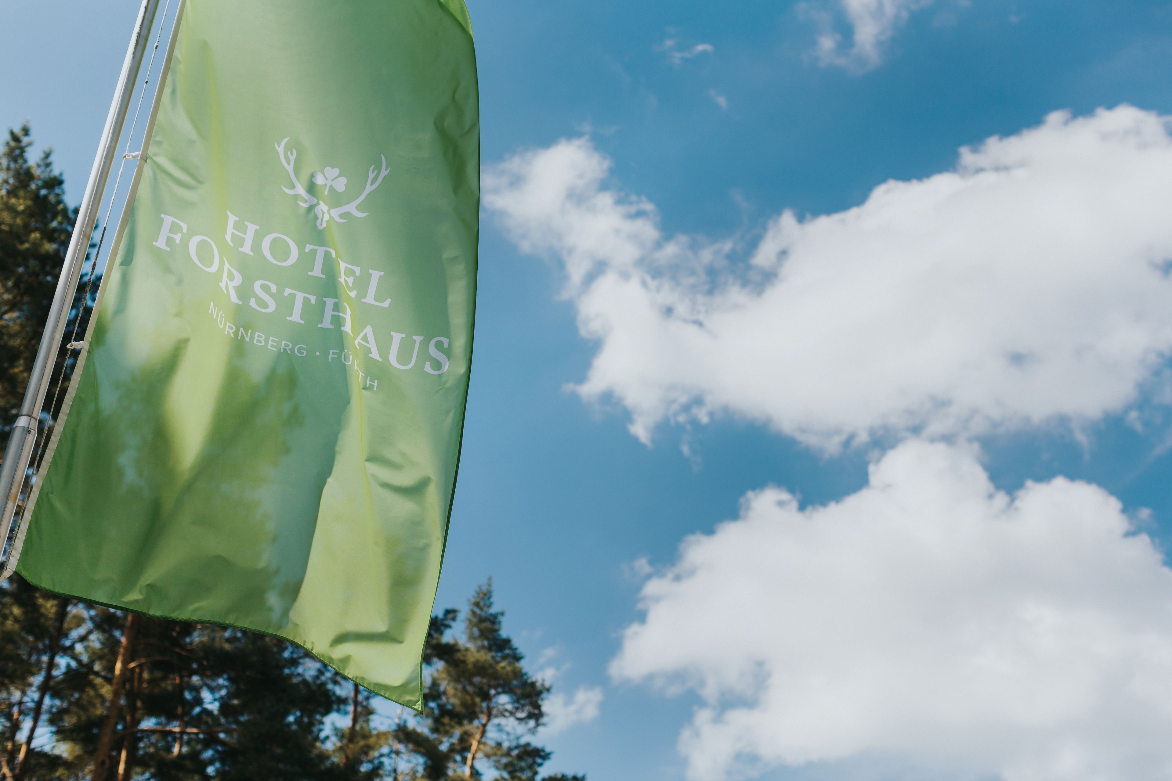 A flag with the text "HOTEL FORSTRAUS" and "NURNBERG - FÜHRTH" against a clear sky with clouds.