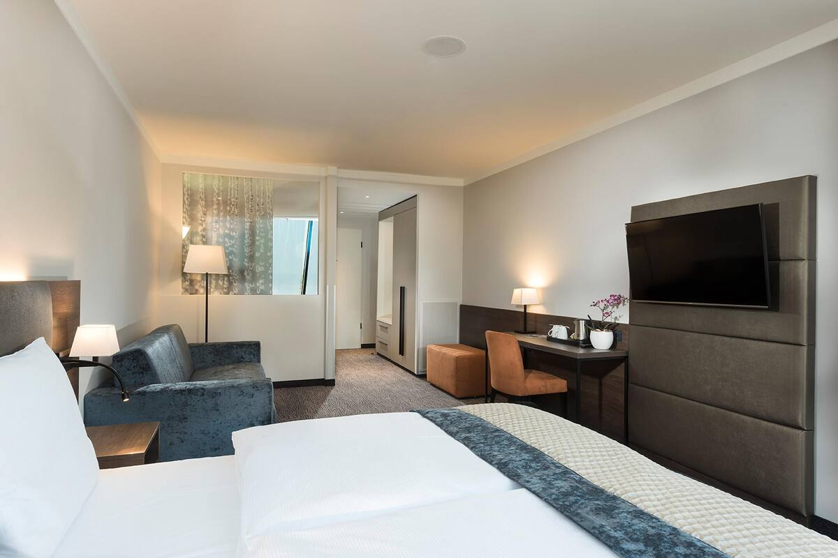 Ein Hotelzimmer mit Bett, Schreibtisch, Stuhl, Fernseher und Lampe.
