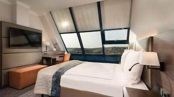 A modern hotel room with a large bed, a flat-screen TV, a desk, and a window with a city view.
