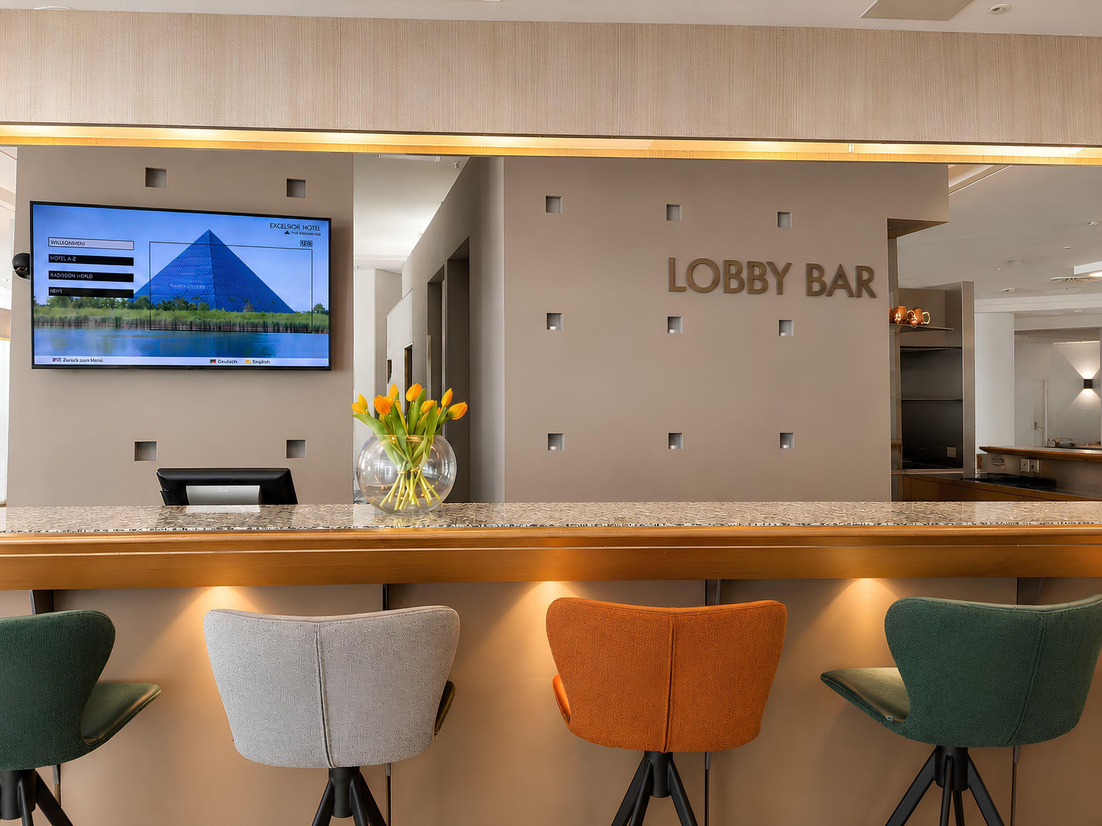 A lobby bar area with a reception desk, a flat-screen TV, and a vase with flowers.
