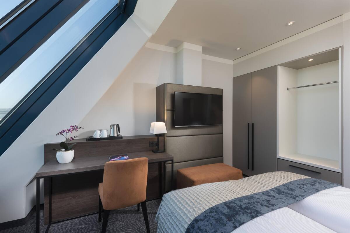 Ein Hotelzimmer mit Bett, Schreibtisch mit Stuhl, einem an der Wand befestigten Fernseher und einem Fenster mit Blick.