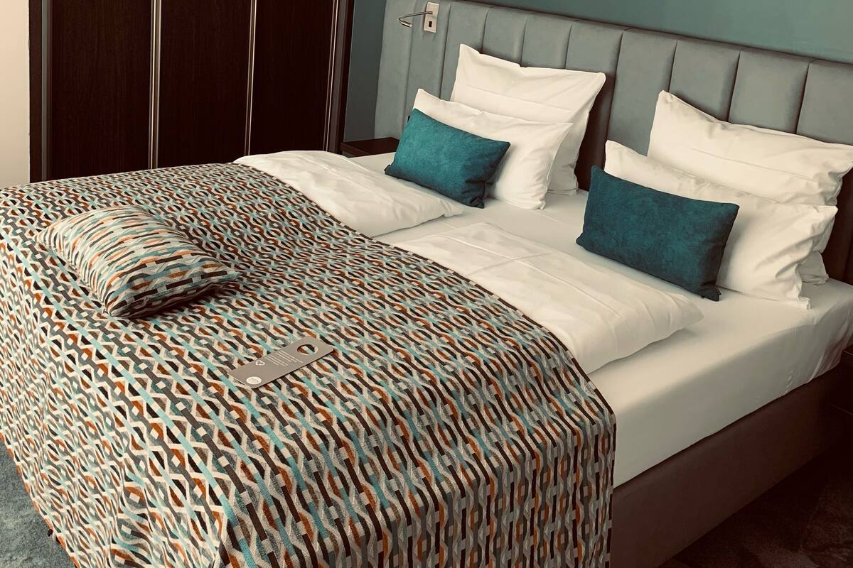 A bedroom with a bed, a patterned bedspread, a headboard, and a wall-mounted mirror.