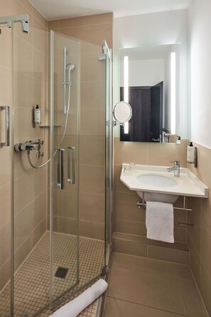 A modern bathroom with a glass-enclosed shower, a white sink, and a large mirror. - Hotel du Nord Alster (Hamburg)