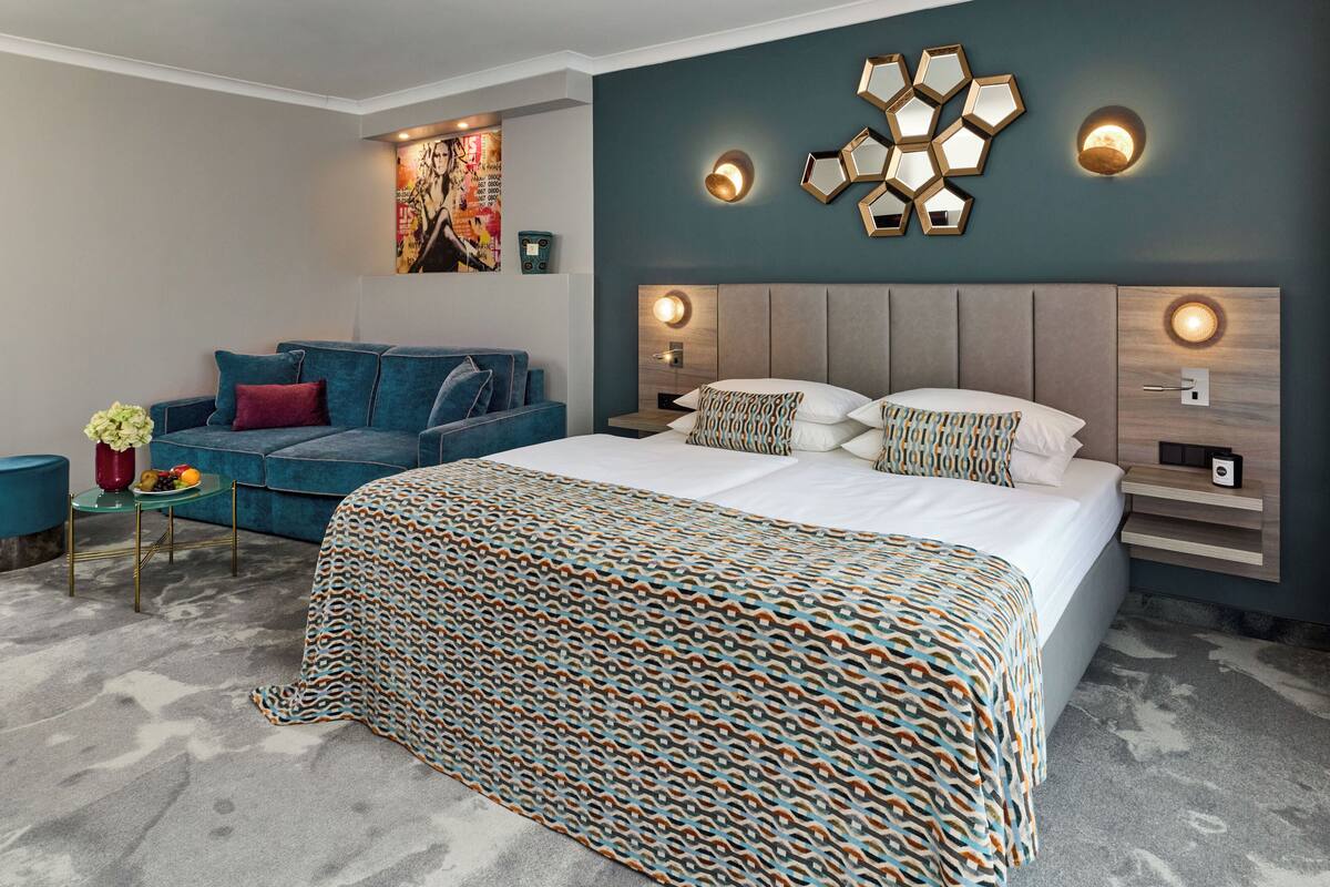 A modern bedroom with a large bed, a sofa, and a small table with a vase and fruit.