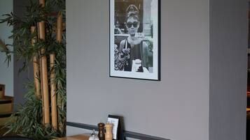 A dining area with a wooden table, black chairs, a framed black and white photo on the wall, a bamboo plant, and a menu stand.