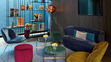 Un salón moderno con una pared azul, un sofá azul, un reposapiés rojo, una silla amarilla y una mesa verde con tapa de vidrio.