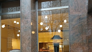 A building facade with large windows, a visible interior with a kitchen area, and a tiled ground. - Hotel Alster-Hof (Hamburg)