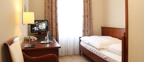 Une chambre d’hôtel comprenant un lit, un bureau avec une chaise, une télévision et une fenêtre avec des rideaux.