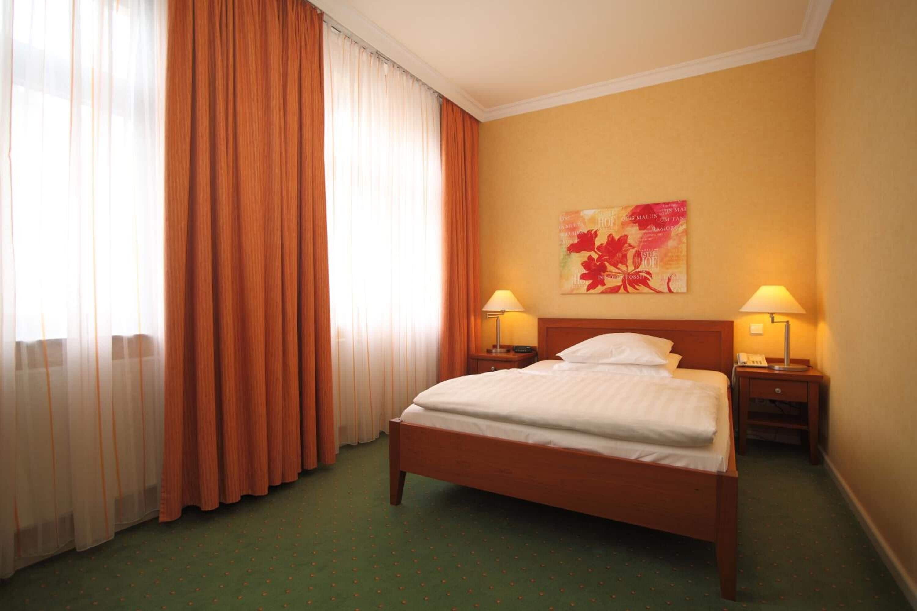 Habitación de hotel con una cama grande, dos mesitas de noche con lámparas, un cuadro en la pared y una ventana con cortinas.
