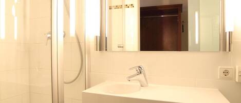 Une salle de bain moderne avec une douche à parois de verre, un lavabo blanc et un miroir au-dessus.