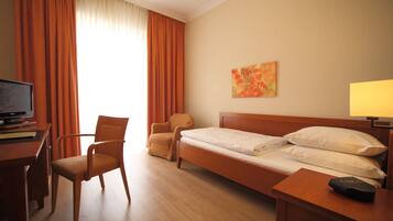 A hotel room with a wooden bed, a desk with a television, a chair, and a painting on the wall.