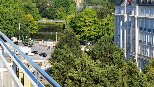 A view of a tower with a spiral design, surrounded by lush green trees and a body of water. - Hotel Alster-Hof (Hamburg)