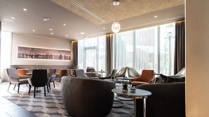 A modern hotel lobby with a geometric patterned floor, comfortable seating, and large windows offering city views. - Hotel Panorama Harburg (Hamburg)