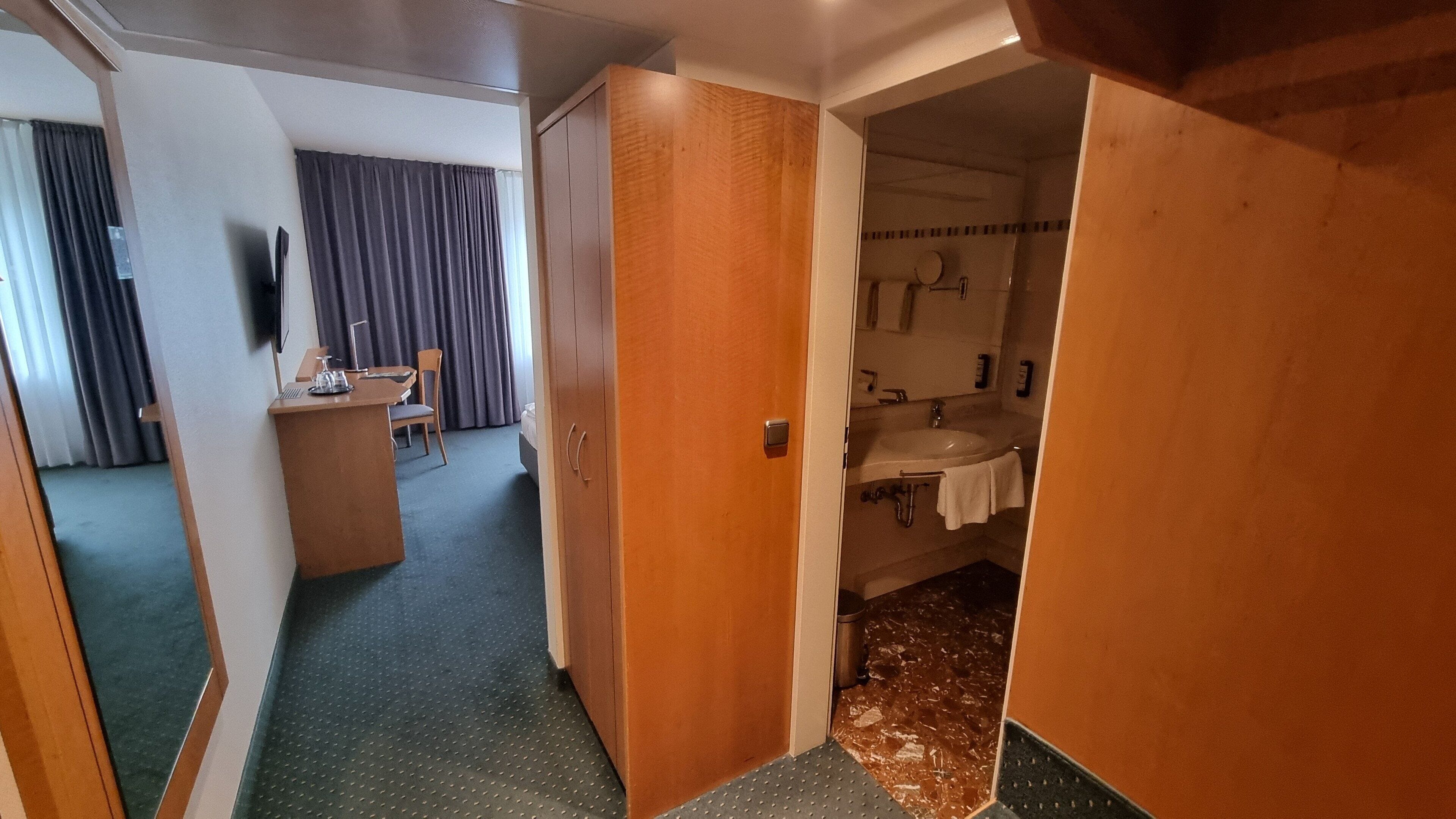 Ein Hotelzimmer mit Schreibtisch, Stuhl und Blick auf ein Badezimmer mit Waschbecken und Spiegel.