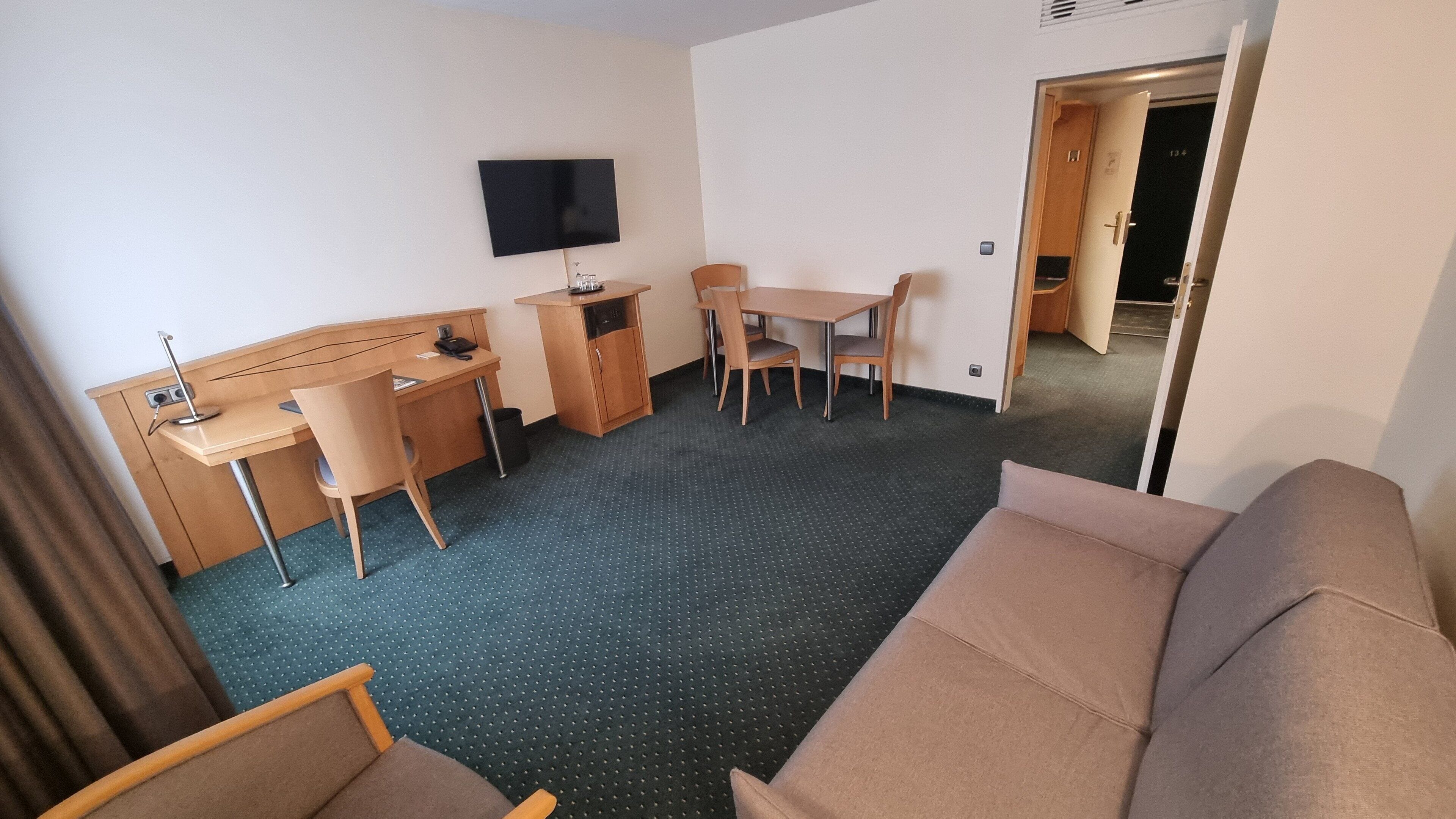 A hotel room with a sofa, a desk with a chair, a television, and a small kitchenette.