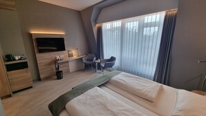 A hotel room with a bed, a desk, a chair, a TV, and a large window with curtains. - Hotel Panorama Harburg (Hamburg)