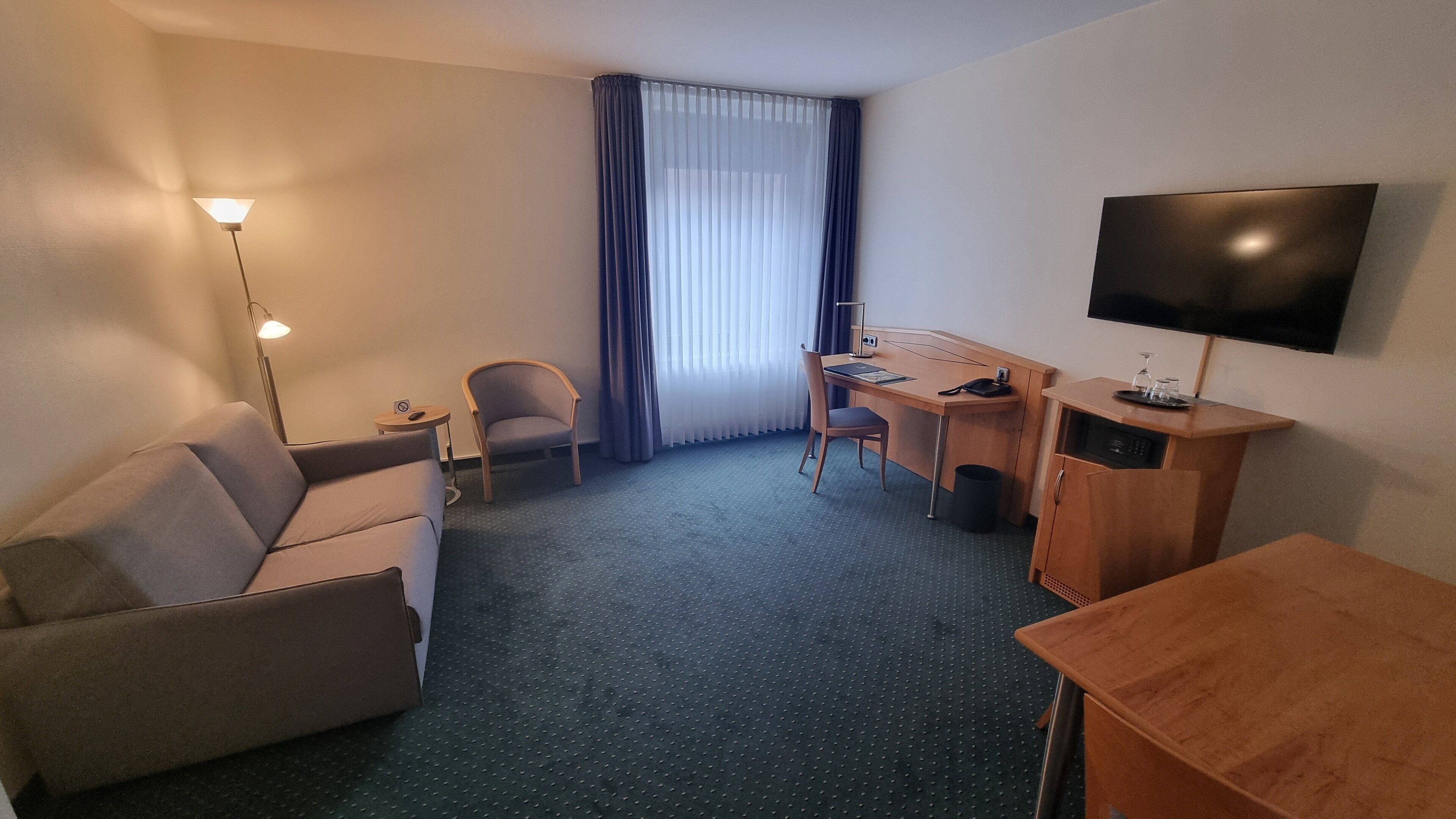 A hotel room with a sofa, a desk, a chair, a TV, and a small table.
