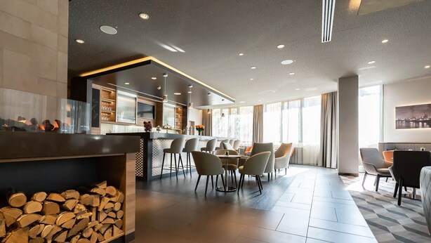 A modern hotel lobby with a bar area, seating, and a fireplace. - Hotel Panorama Harburg (Hamburg)