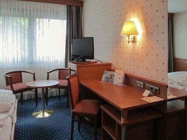 A hotel room with a bed, a desk, a television, a small table, two chairs, and a lamp. - Hotel Helgoland (Hamburg)