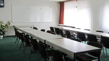 A conference room with a long table, chairs, a whiteboard, and a potted plant.