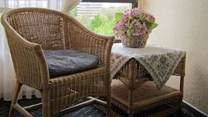 A wicker chair with a cushion, a small table with a patterned tablecloth, and a vase of flowers. - Hotel Helgoland (Hamburg)
