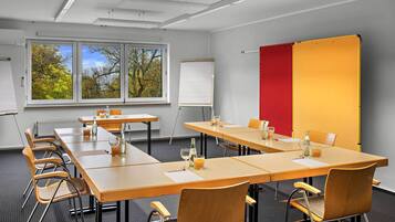 A conference room with long tables, chairs, a whiteboard, and a large window with a view of trees.