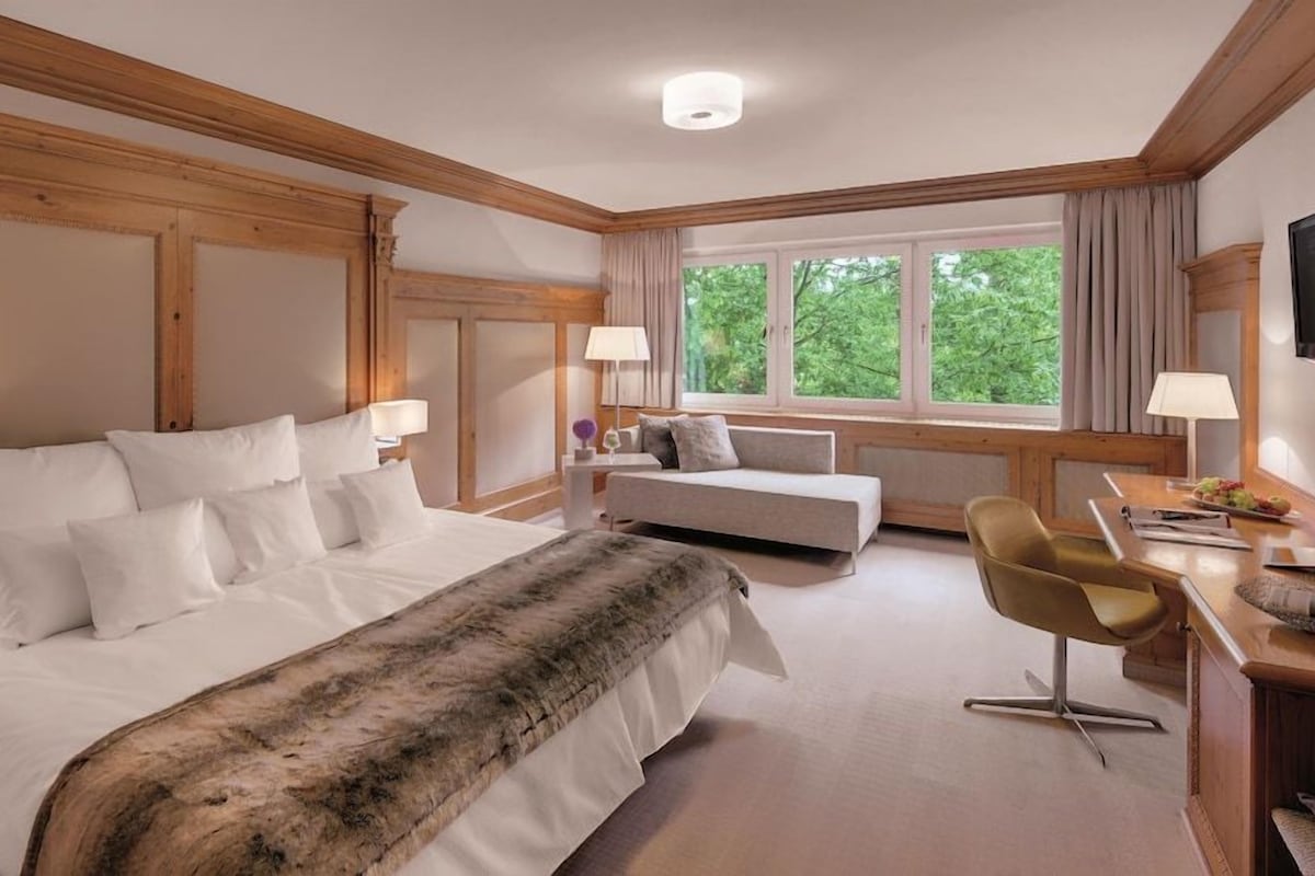 Habitación de hotel con una cama grande, un escritorio con silla, un televisor y una ventana con cortinas.