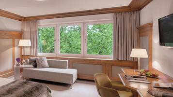 Una habitación de hotel con cama, sofá, escritorio con silla, televisor y ventana con cortinas.
