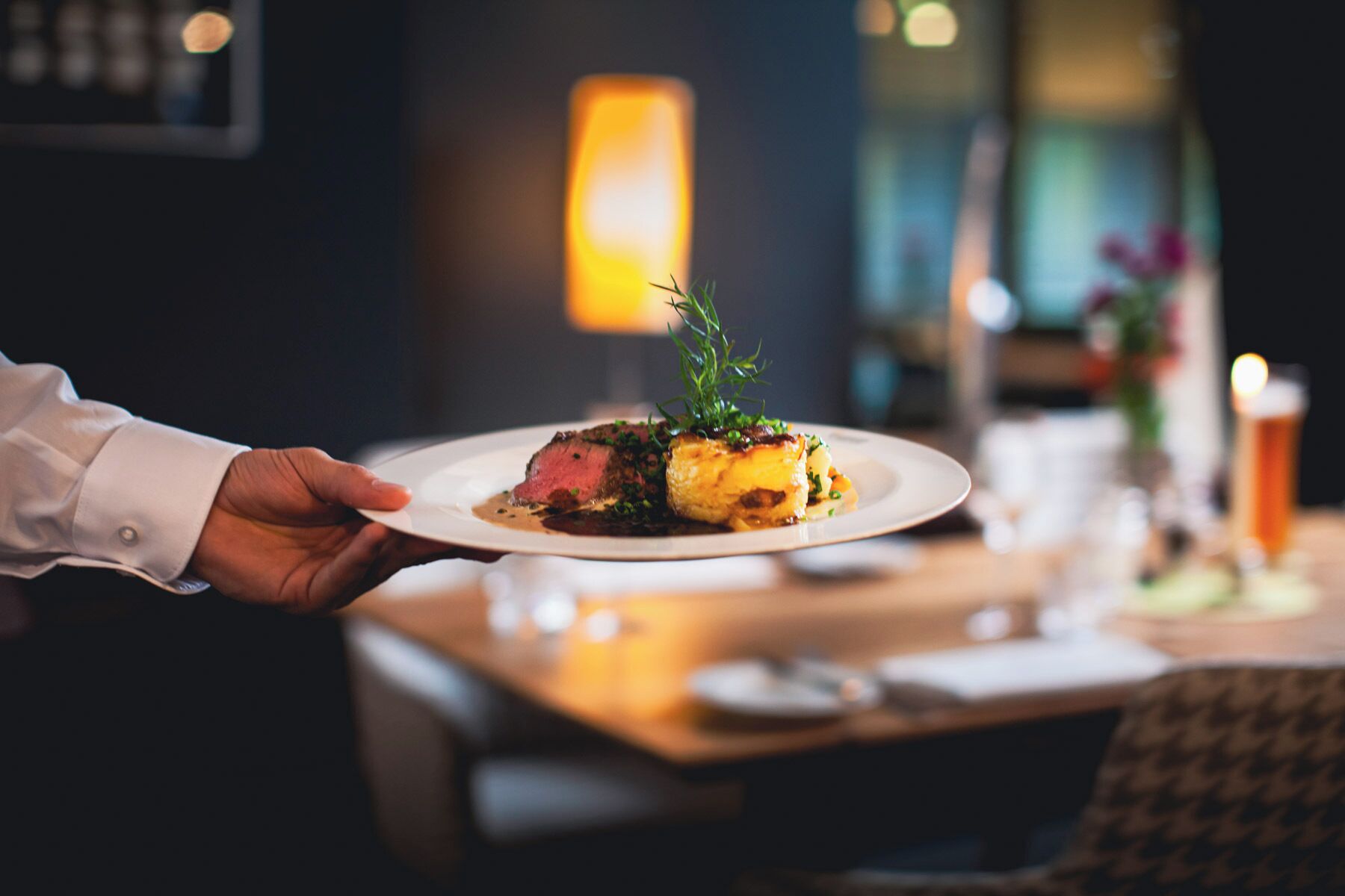 Una persona sosteniendo un plato con un bistec y verduras, en un restaurante con poca luz.