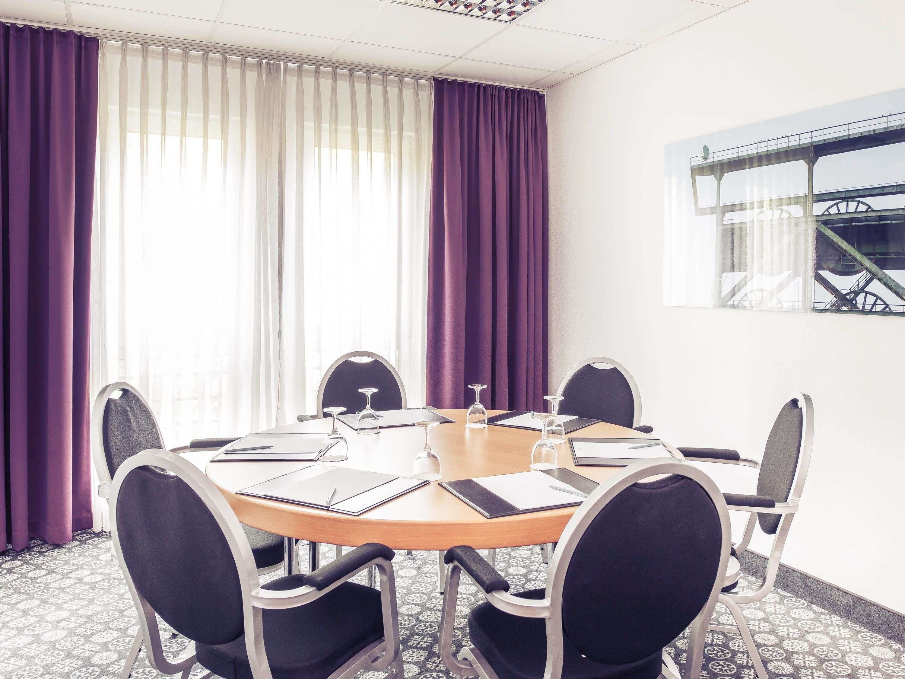 A conference room with a round table, six chairs, and a window with a view of a bridge.