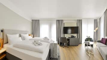 A modern hotel room with a large bed, a desk with a chair, a television, and a sofa.