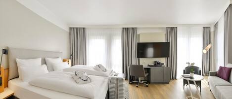 A modern hotel room with a large bed, a desk with a chair, a television, and a sofa.
