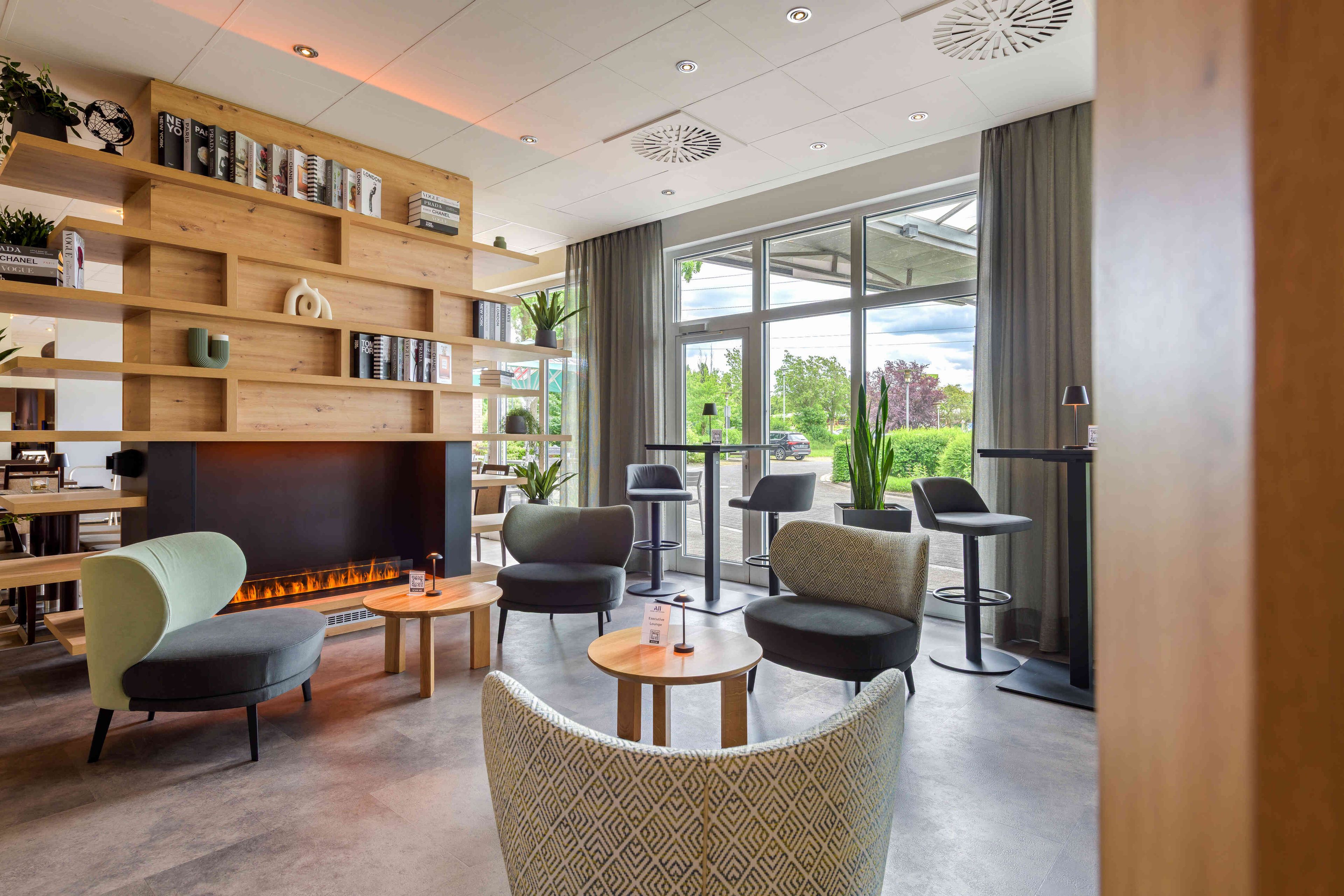 A modern lounge area with a fireplace, comfortable seating, and a bookshelf with magazines.
