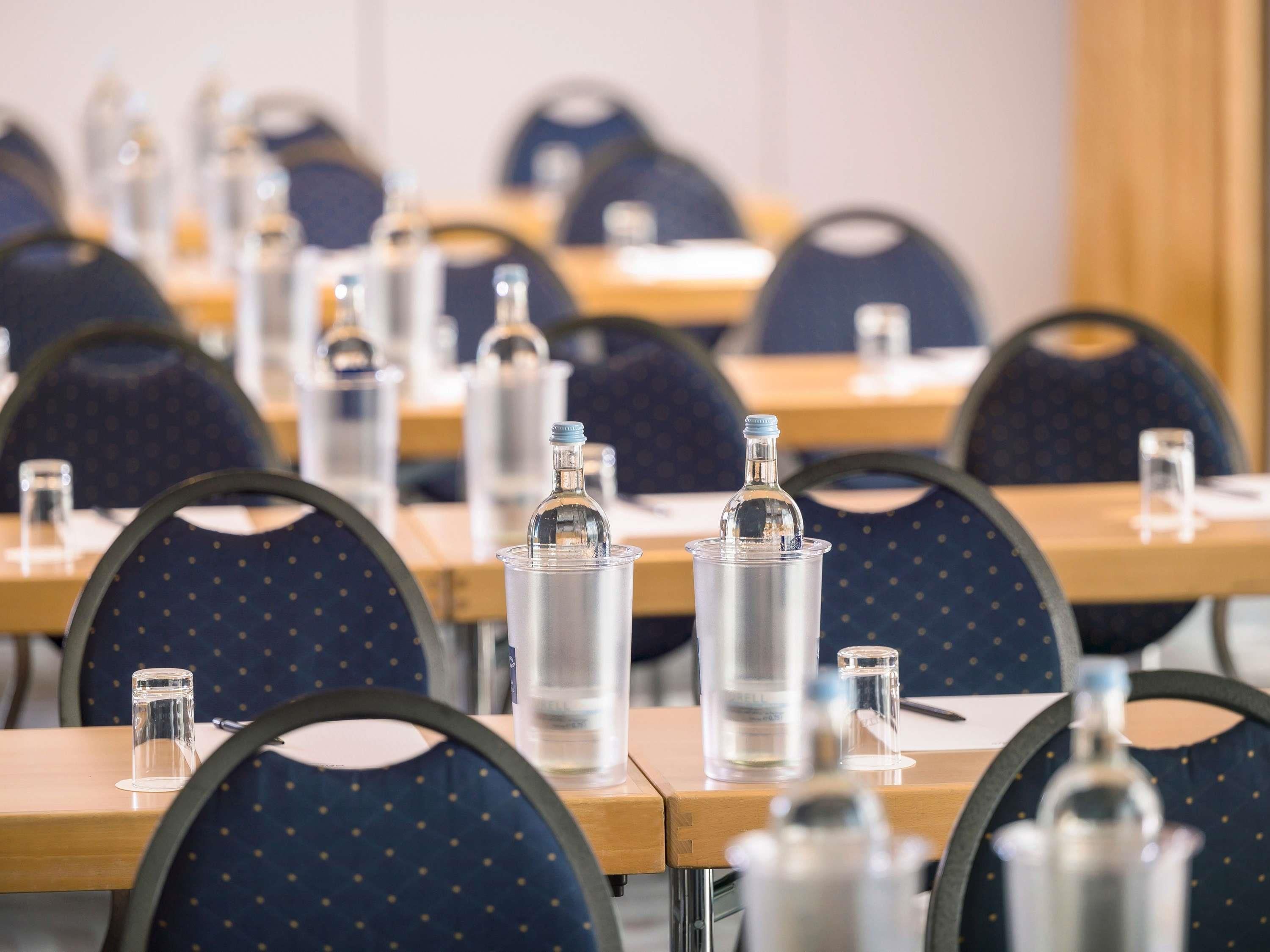 Un salón de conferencias con mesas, sillas y botellas de agua.