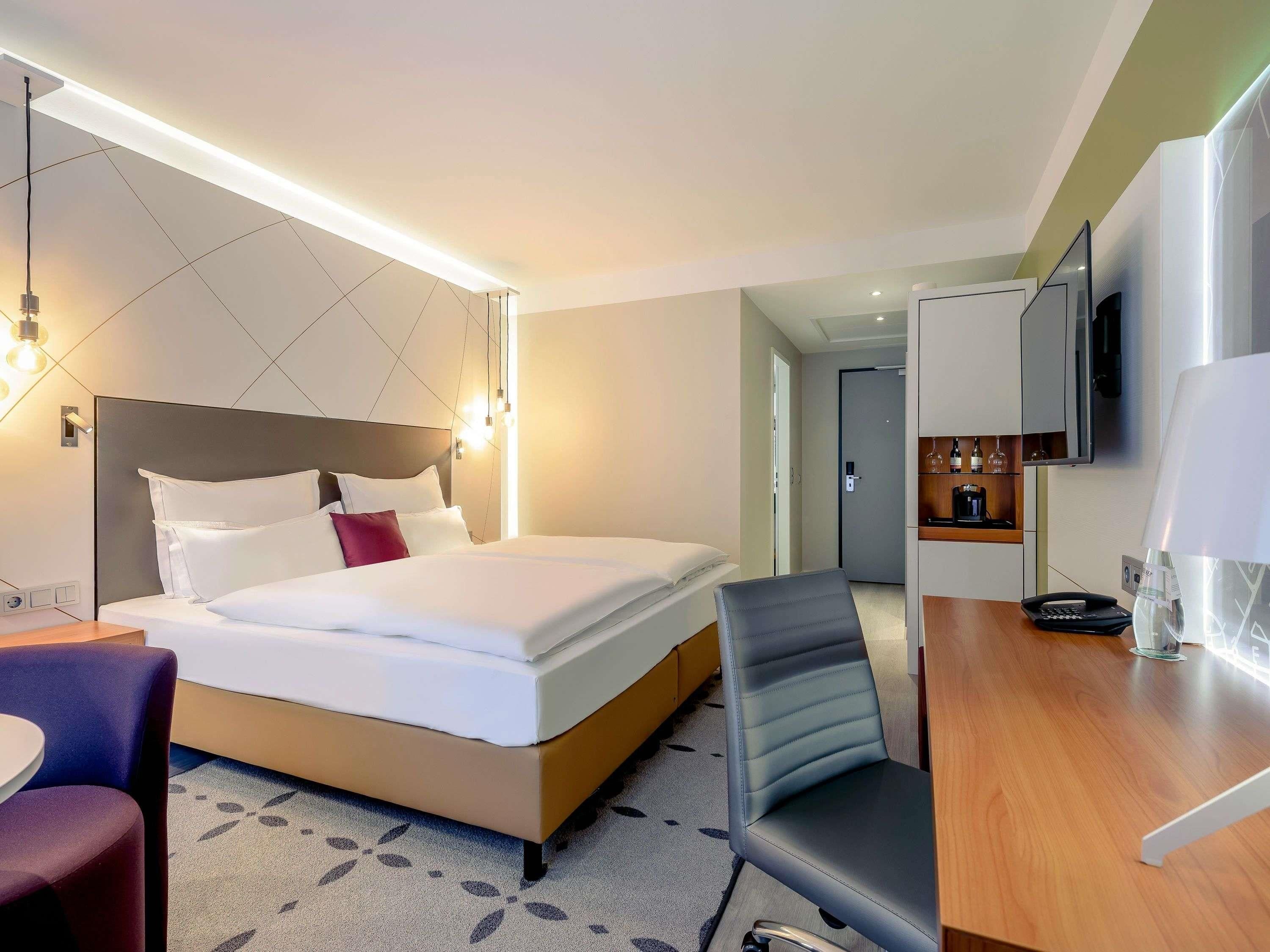 Habitación de hotel con cama, escritorio, silla, televisor y minibar.