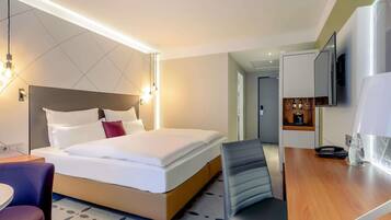 Habitación de hotel con cama, escritorio, silla, televisor y minibar.